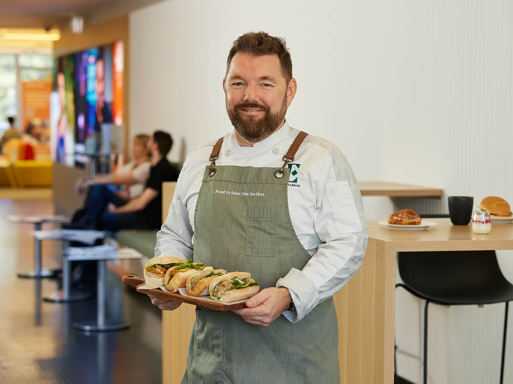 chef smiling at camera holding freshly made food in cafe setting
